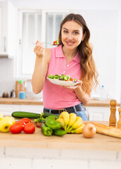 Smiling young woman enjoying salad at home