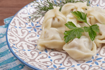 Cooked dumplings decorated with a fresh parsley and dill in the plate on checkered napkin on the table.
