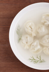 Bouillon with homemade pelmeni and fresh dill. Soup with dumplings and herbs. Top view.