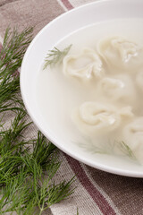 Bouillon with homemade pelmeni and fresh dill. Soup with dumplings and herbs on tablecloth.