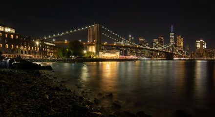 Brooklyn Bridge frames the Manhattan skyline at night, looking south from the dumbo section showing...