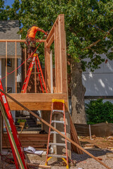 Framing the double top plate on the first floor of a home. The contractor standing on an aluminum ladder to reach the right position to use the nail gun to fasten the pieces