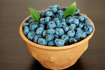 A full jug of fresh large blueberries with leaves on a dark background. Berries, healthy food. Selective focus. Side view.