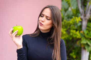 Young pretty woman with an apple at outdoors with sad expression