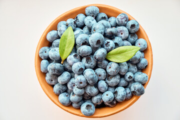 A full jug of fresh large blueberries with leaves on a white background. Berries, healthy food. Selective focus. View from above.