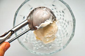 A human hand puts a scoop of ice cream into a glass bowl with a scoop. Close-up
