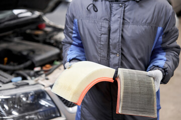 New and old dirty automotive engine air filter in the hands of an auto mechanic. Auto repair concept.
