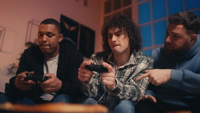 Three young men playing video game using joysticks, friends hanging out at home
