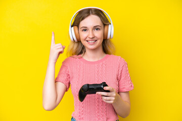 Blonde English young girl playing with a video game controller isolated on yellow background pointing up a great idea