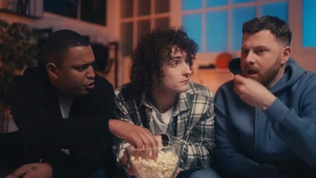 Group of male friends eating popcorn while watching movie together, relaxation