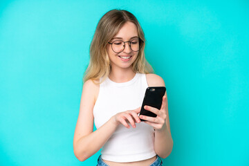 Blonde English young girl isolated on blue background sending a message or email with the mobile