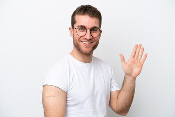 Fototapeta premium Young caucasian man wearing band aids isolated on white background saluting with hand with happy expression