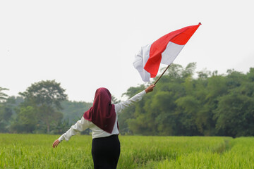 Asian woman in white shirt waving Indonesian flag excitedly in rice field.