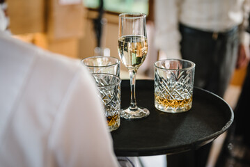 Waiter serves and carries a tray with glasses of champagne, whiskey, scotch, whisky, brandy. Party and holiday celebration. Catering service concept. Closeup. Waiter receives guests in restaurant.