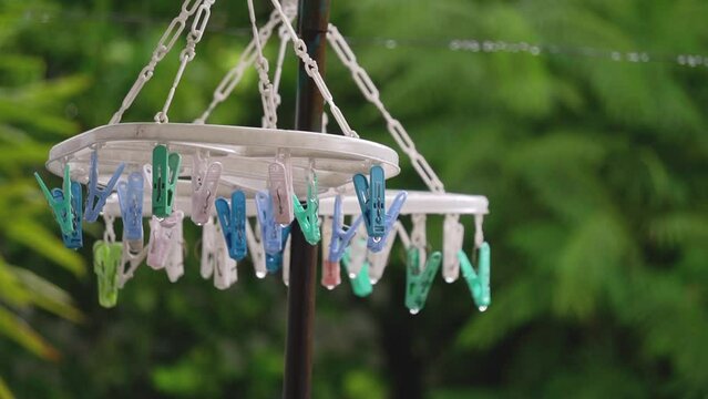 Tele closeup of two racks of plastic, various color clothespins with green trees, branches, and nature background on a rainy day.