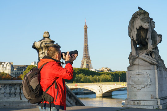 View tourist photographer taking picture of statue on Pont Alexandre III bridge in morning sunlight