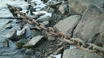 A rusty chain hangs over the surface of a frozen winter river