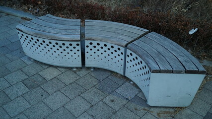 A curved bench separated into three parts in an outdoor park in Seoul in the evening