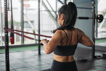 Fototapeta na wymiar Strong Asian woman doing exercise with resistance bands at cross fit gym. Athlete female wearing sportswear workout on grey gym background with weight and dumbbell equipment. Healthy lifestyle.