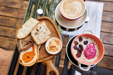 Breakfast with fresh cooked porridge served with Dry Cherry with strawberry sorbet in bowl. Assorted sliced bread on a wooden board. Served with smoked butter. Breakfast with cappuccino coffee.