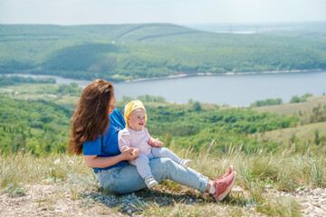 A mother holds a toddler child on top of a mountain with a beautiful view of the mountains and the Volga River, Russia