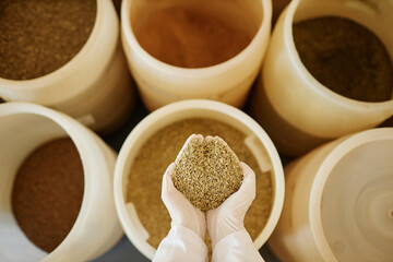 Top view background image of hands holding rye seeds and crops over tanks in food factory, copy space