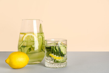 Glass and jug of lemonade with cucumber on grey table