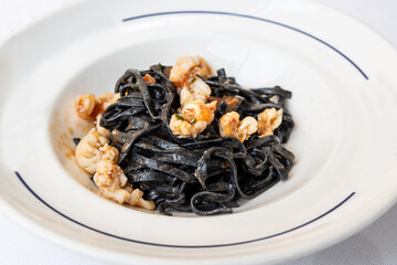 Serving portion of Italian squid ink pasta with shrimps served in white plate