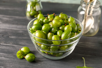 Glass bowl with fresh gooseberries on black wooden table