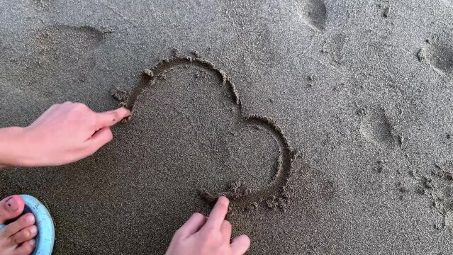 A kid draw a heart shape on the sand, puppy love concept.