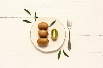 Plate with fresh kiwi and leaves on white wooden background