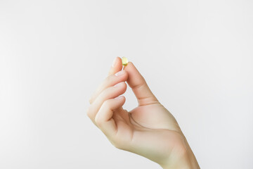 hand holding a yellow vitamin capsule. taking vitamins and nutritional supplements for female beauty and health
