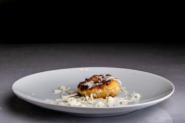 fried cutlet sprinkled with cheese lies on a plate on a black background, isolated