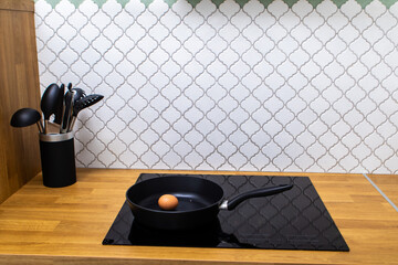 a black frying pan with an egg stands on a stove in a kitchen interior
