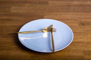 white plate with a golden knife and fork on a wooden tabletop background
