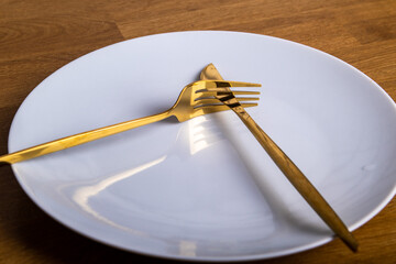 white plate with a golden knife and fork on a wooden tabletop background