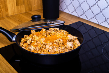 turkey goulash in a frying pan on a stove in a kitchen interior