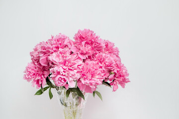 A large lush bouquet of pink peonies in a vase on a white wall background - 626576635