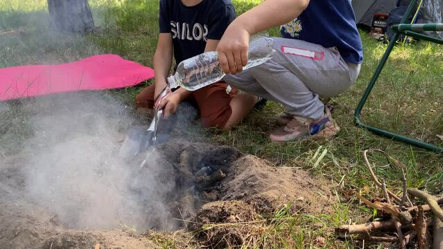 Responsible kids take charge, carefully extinguishing campfire while family hiking adventure in forest. Boy buries embers with soil, girl pours water, ensuring safe end to camping experience at nature