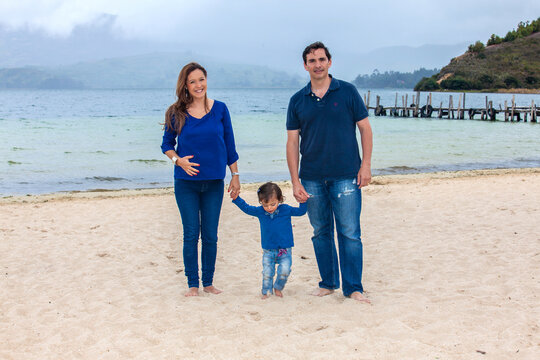 Young couple waiting for their second baby having fun with their baby girl at the beautiful white beach of Lake Tota located in the department of Boyaca at 3,015 meters above sea level in Colombia