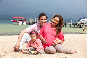 Young couple waiting for their second baby having fun with their baby girl at the beautiful white beach of Lake Tota located in the department of Boyaca at 3,015 meters above sea level in Colombia