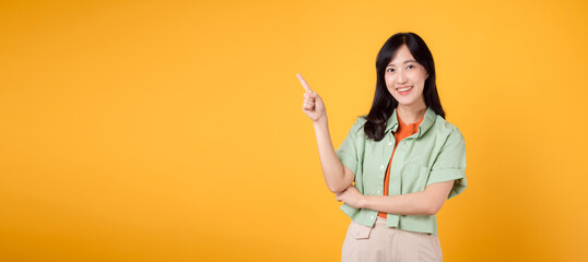 young 30s Asian woman wearing a green shirt on an orange shirt, pointing with excitement to free...