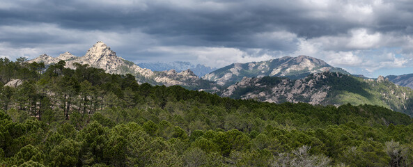 Panorama sur l’Alta Rocca dans les montagnes Corses au sud de l’île. La roche de la montagne contraste avec la forêt sous un ciel d’orage menaçant. 