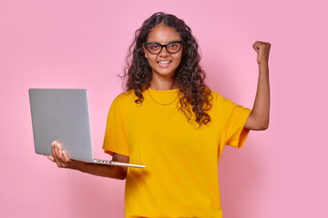 Young overjoyed attractive Indian woman teenager holding laptop and making winning gesture after...