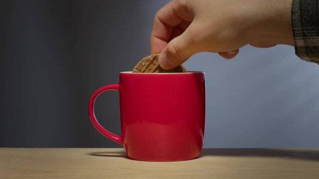 A Man's Hand Dunks A Biscuit - Cookie - Into A Hot Beverage In A Bright Red Coffee Mug.