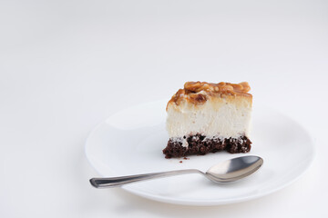 A piece of cheesecake with peanuts and caramel on a white plate with a spoon on a white background