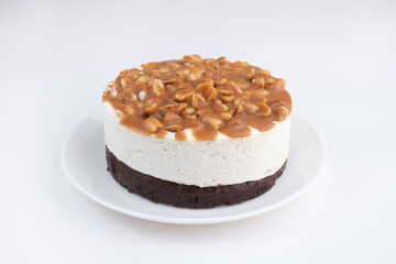 heesecake with peanuts and caramel on a white plate on a white background