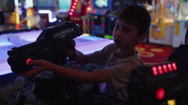 Boy plays an arcade with a toy gun in an entertainment center against the backdrop of slot machines