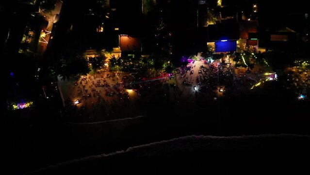 Row of seaside beach nightclubs aerial view from water. Sea front cafes and restaurants colourful lights at night, crowd dances at disco by sea at Christmas celebration party down view from drone
