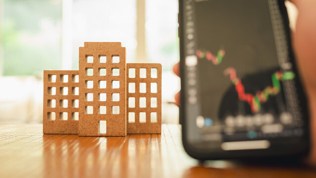 Wooden house, business building model on wood background with a businessman 's hand looking at a stock chart. Investment , a symbol for construction , ecology, loan, mortgage, property or home.